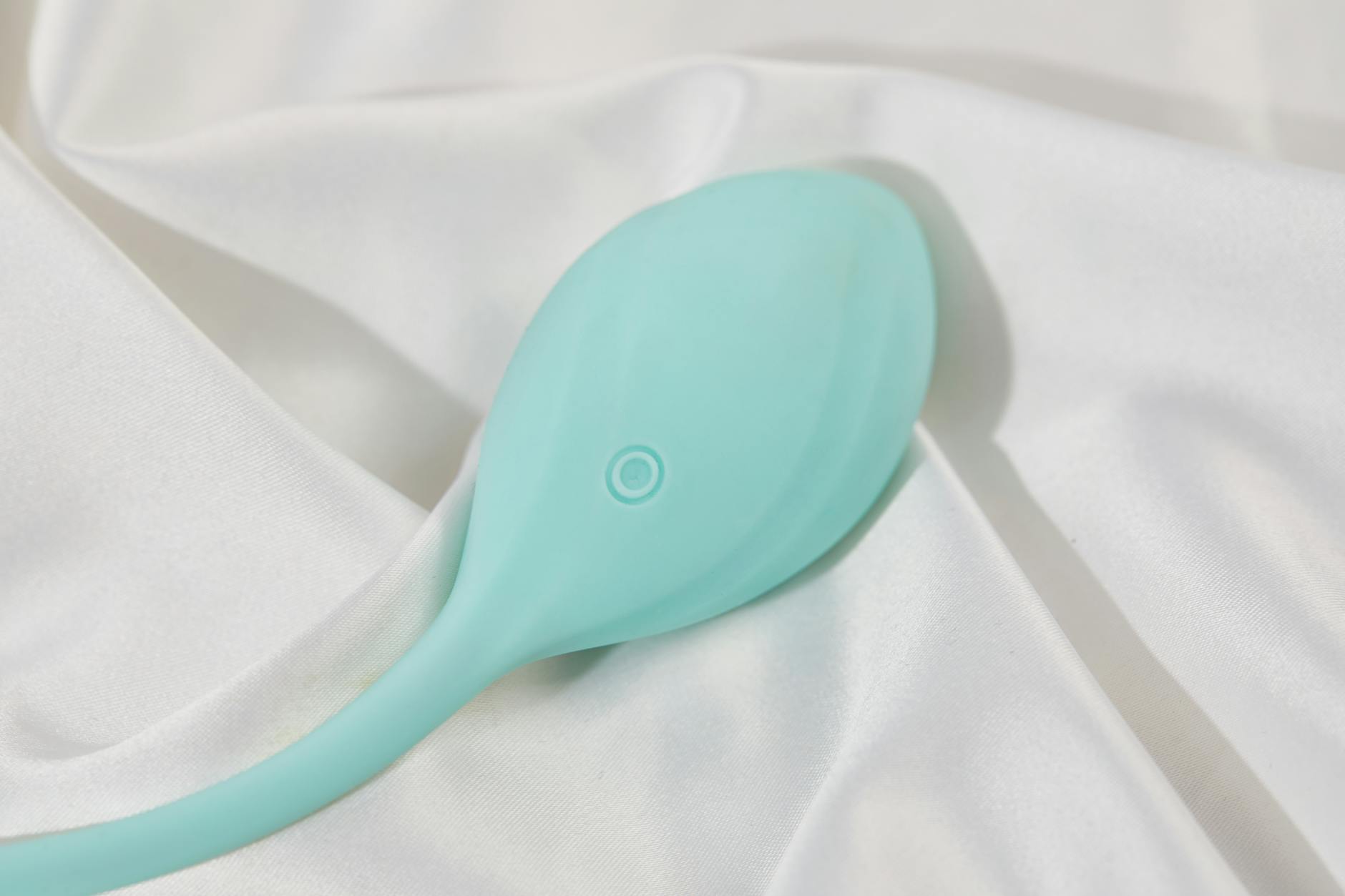 A teal lemon clitoral vibrator resting on white silk fabric, symbolizing self-care and gentle reconnection