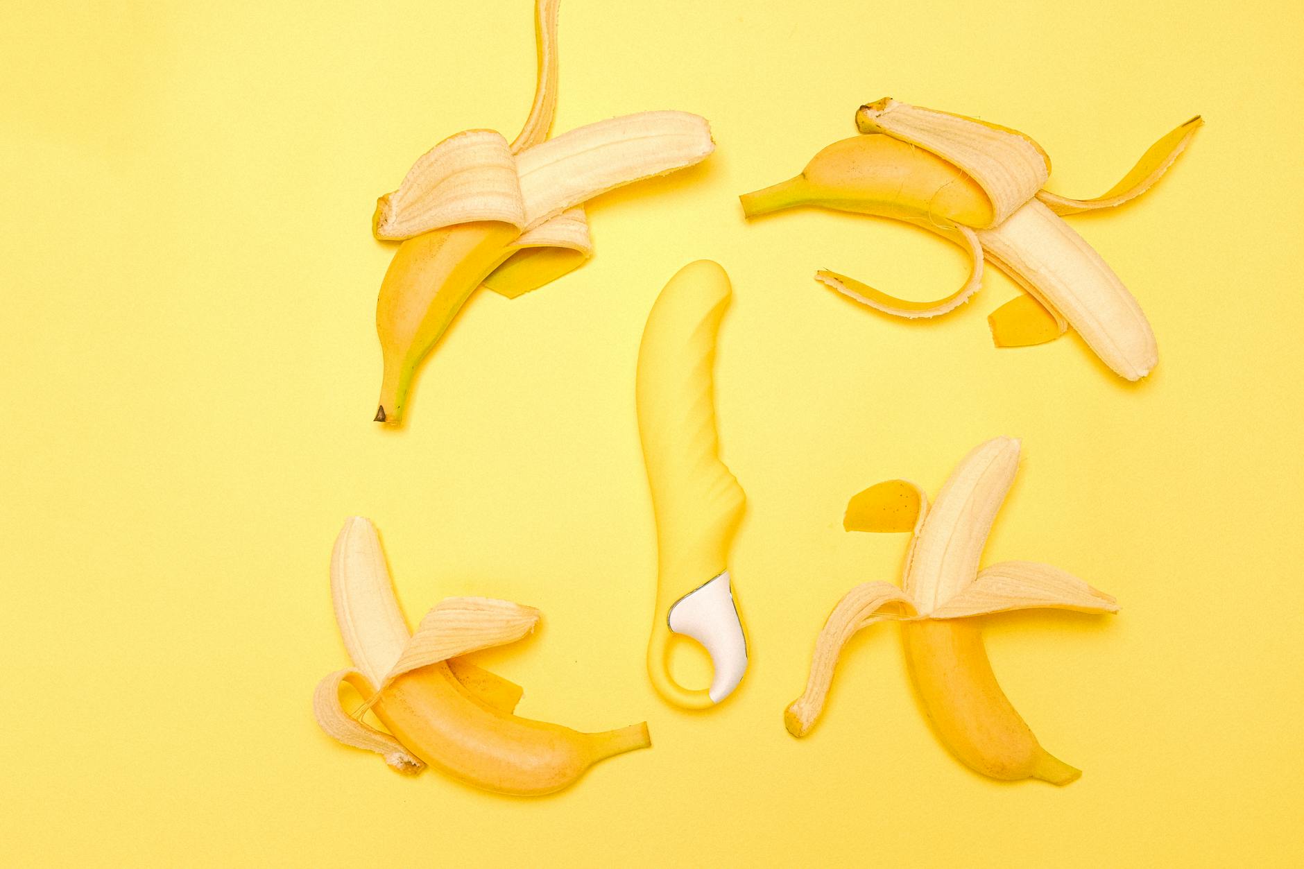 Yellow silicone clitoral vibrator surrounded by peeled bananas on a bright yellow background