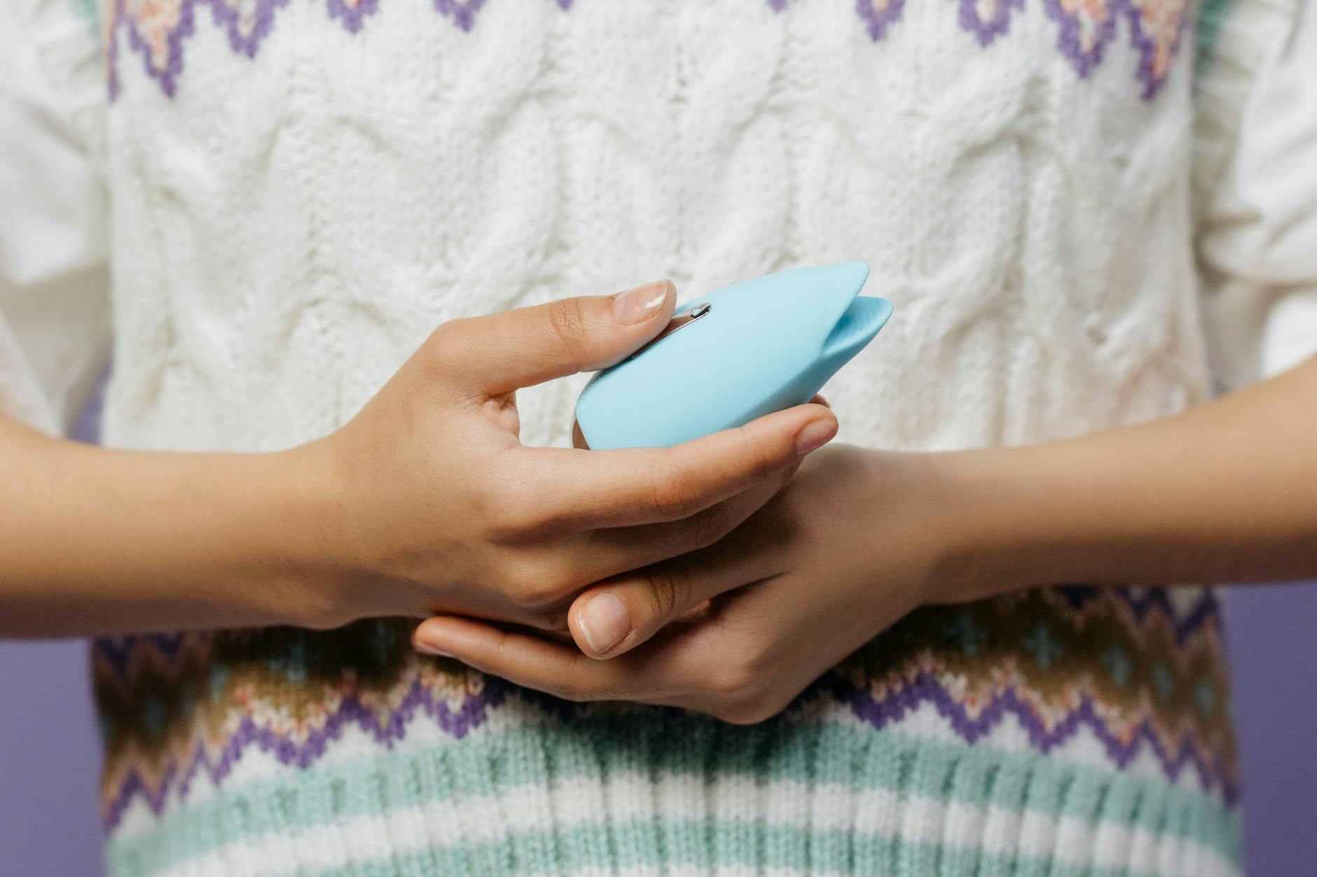 A blue silicone vibrator held in hand against a solid purple background, representing modern intimacy and self-care